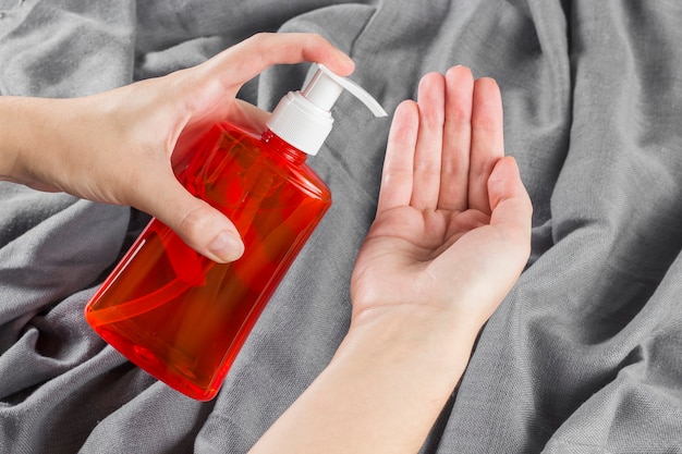 Female hand applying alcohol on a gray fabric background.