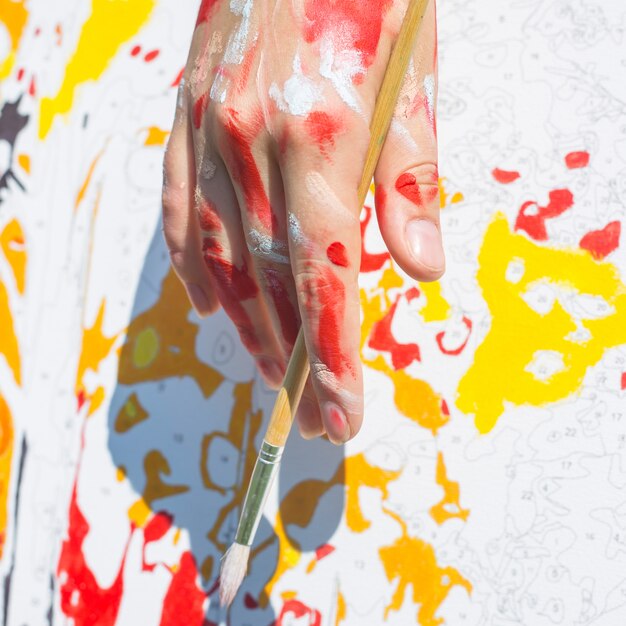 The female hand of the artist smeared in paint holds a brush. 