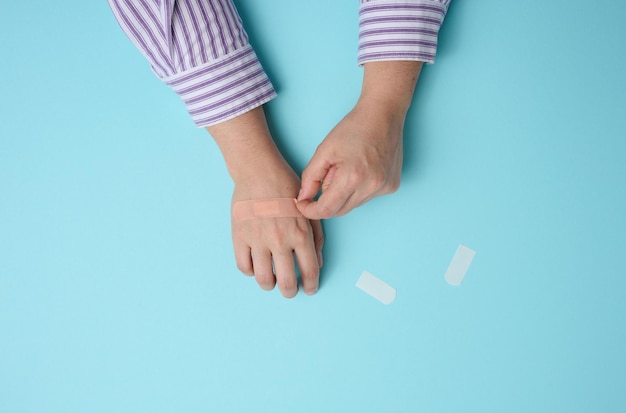 Female hand and brown medical adhesive plaster for the treatment of injuries and cuts on the skin blue background