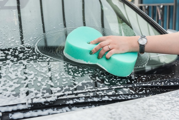 Female hand cleaning car in service with tools soap foam and water. wash auto