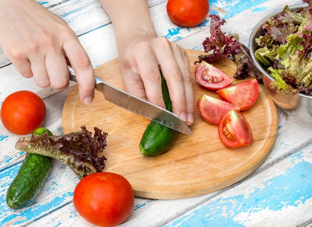 Female hand cutting cucumber and making salad