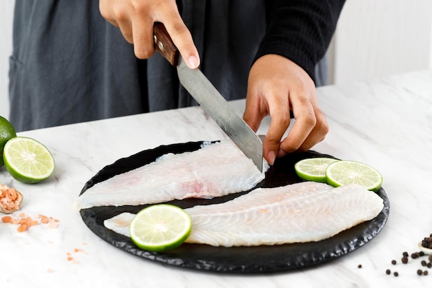 Photo female hand cutting dori fillet pangasius fish above stone board process cooking in the kitchen