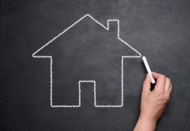 A female hand drawn with chalk on a blackboard a miniature house concept of rent mortgage