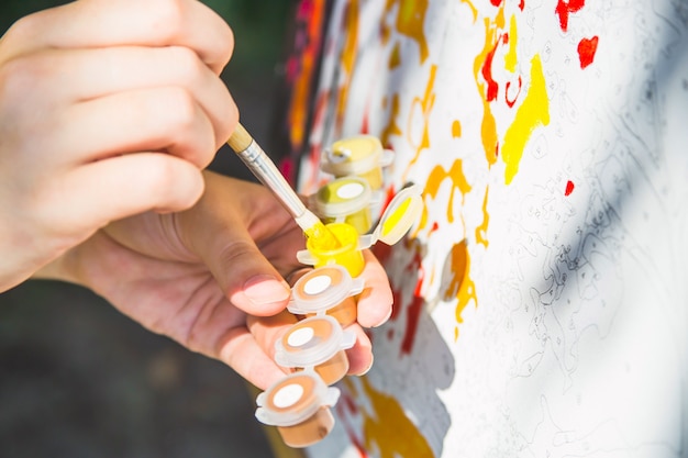 A female hand dunks a brush in yellow paint to draw on the canvas with numbers