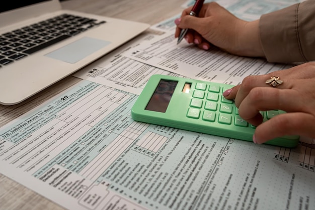 Female hand filling US tax form 1040 with help calculator and laptop in the office