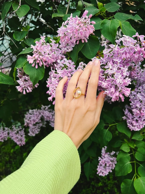 Female hand in a green jacket and golden jewelry ring  holds a lilac flower.