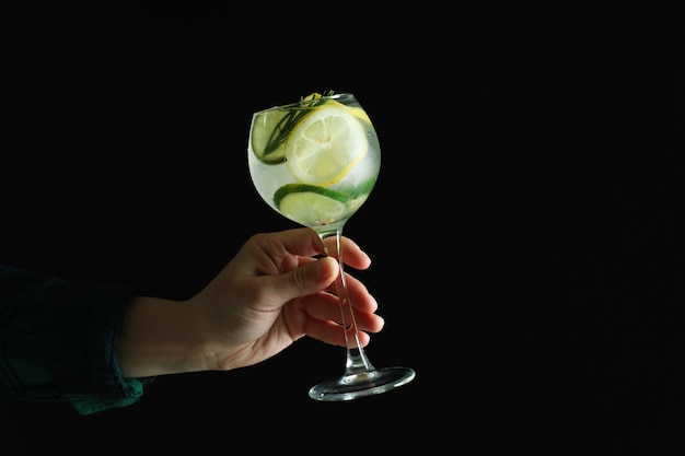 Female hand hold glass of cocktail with citrus on dark surface