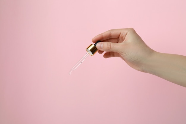 Female hand hold pipette with pine oil on pink