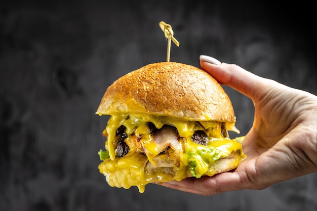 Female hand holding a big appetizing bitten burger on a dark concrete background fast food and junk food concept place for text