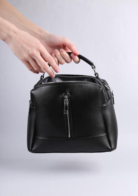 Female hand holding black leather bag on gray background