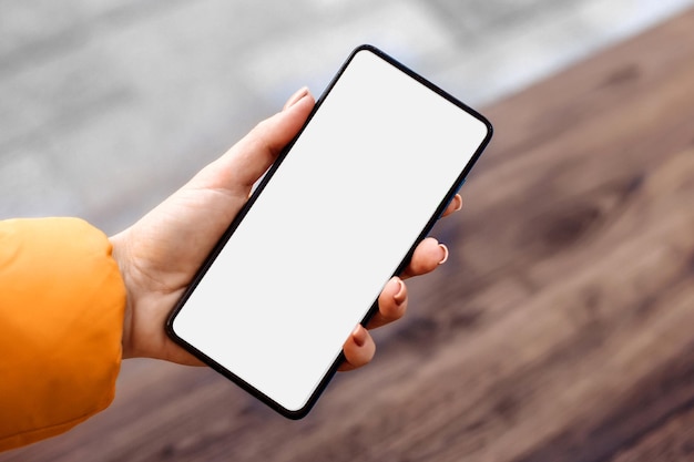 Female hand holding black mobile phone with white empty screen. Mockup for design