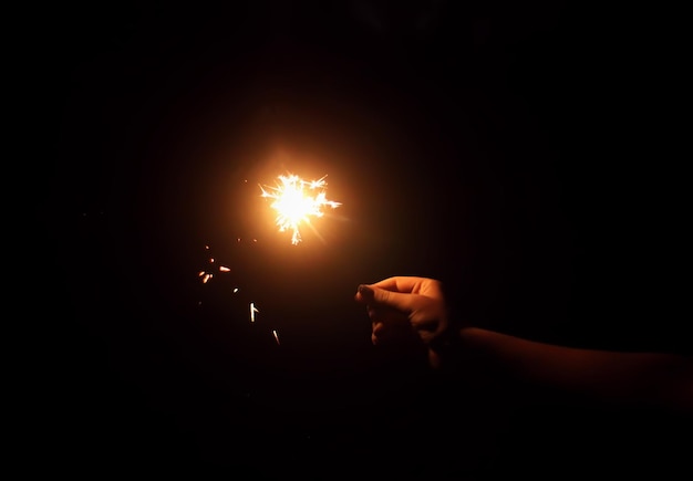 Female hand holding a burning sparkler on night darkness background