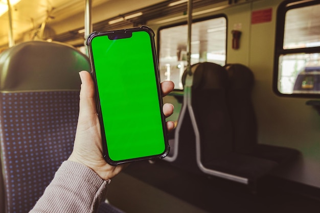 Female hand holding chroma key screen phone in the train Social Network Work and Travel phone with blank copy space screen for your text message New Apps Smartphone with Green Screen Mock Up Display