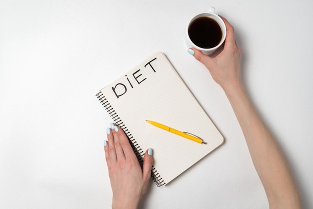 Female hand holding a cup of coffee a notebook with the title Diet Preparation menu concept