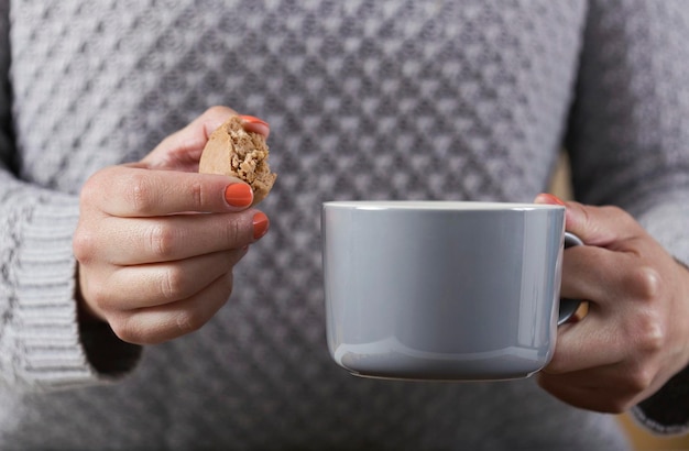 Female hand holding a cup of coffee and in the other a french macaroon