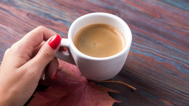 Female hand holding cup of coffee with autumn leaf