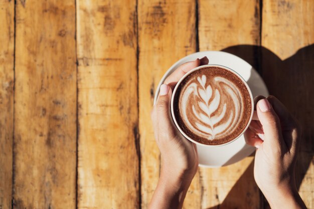 Female hand holding cup of hot cocoa or chocolate on wooden table, close up