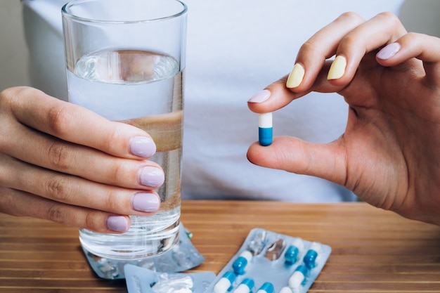 Female hand holding a glass of water and pill