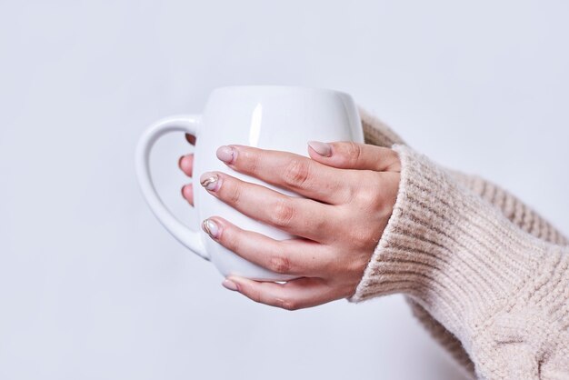 Female hand holding hot tea cup against white background a woman in warm knitted sweater holds in ha...