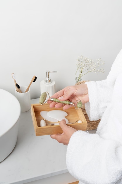 Female hand holding jade massage face roller in bathroom