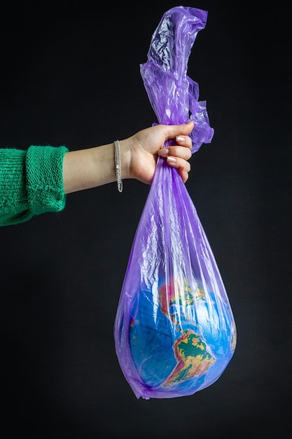 Female hand holding plastic bag with world globe isolated on black background