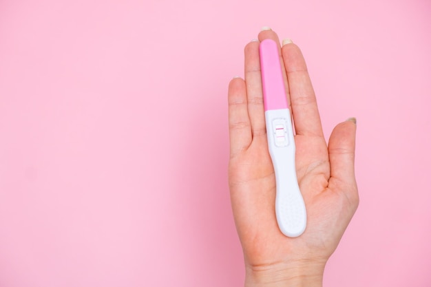 Female hand holding a positive pregnancy test on the pink background