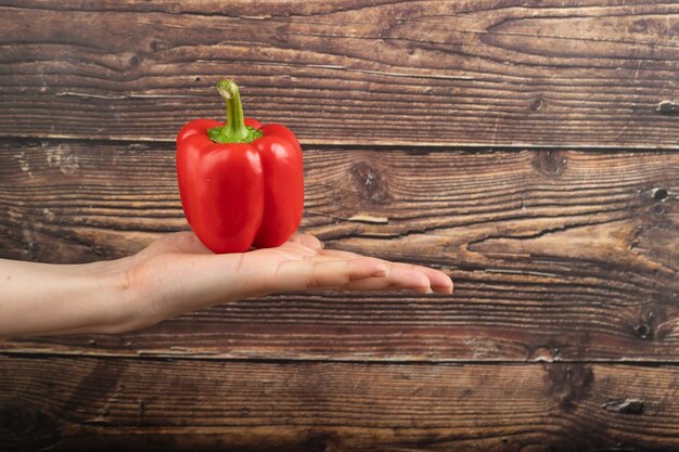 Female hand holding red bell pepper on wooden surface