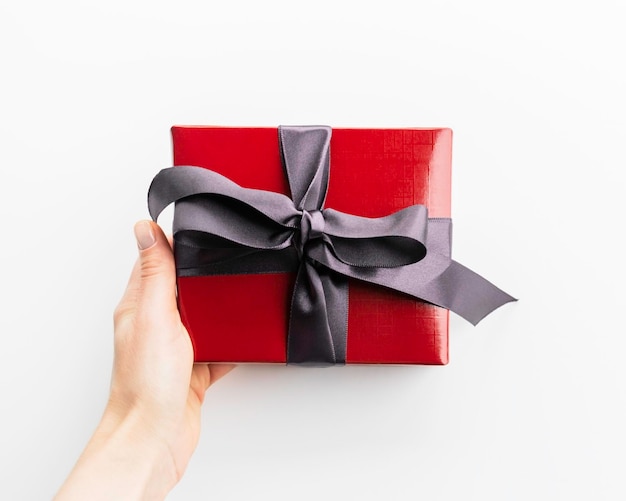 female hand holding red Christmas gift box with gray satin ribbon on white background