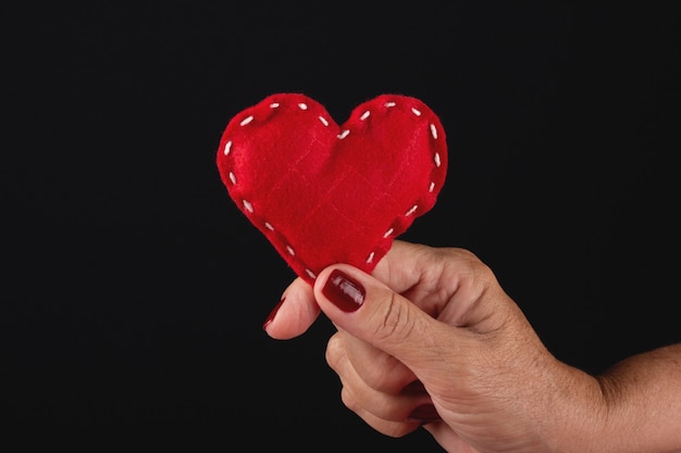 Female hand holding red heart on black background.