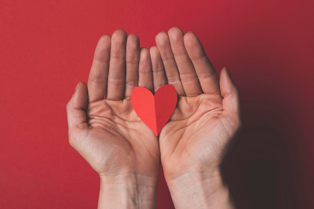 Female hand holding a red paper cut out heart on a plain red background