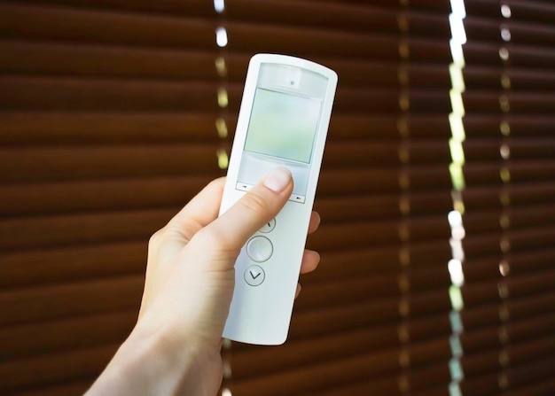 female hand holding remote control to open wooden blinds