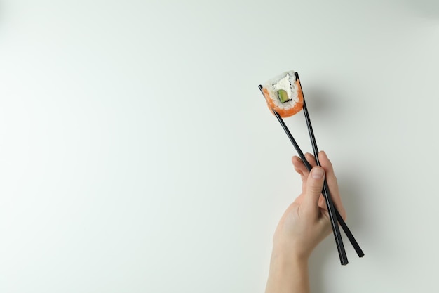 Female hand holding roll with chopsticks on white background