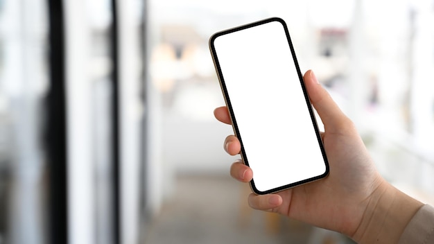 Female hand holding a smartphone white screen mockup over blurred background closeup