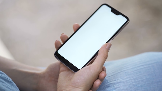 Female hand holding smartphone with white screen. Girl using mobile phone while walking in the autumn park.