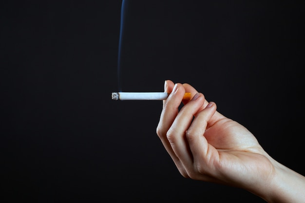 Female hand holding a smoking cigaretteharm from use nicotine close-up.