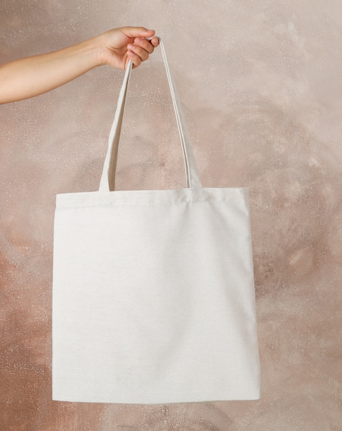 Female hand holding tote bag against brown background