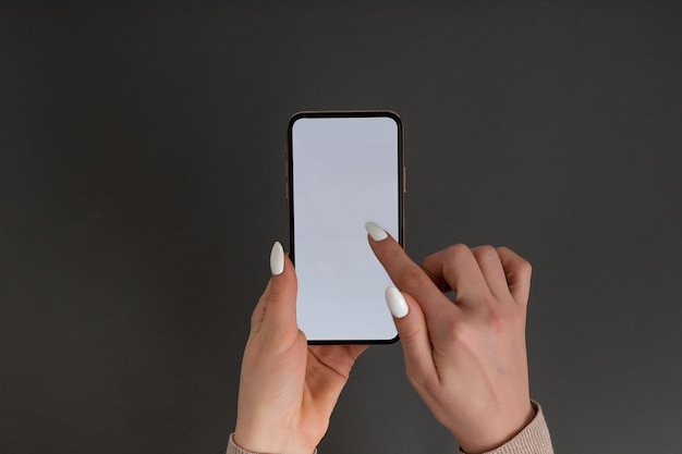 Female hand holding and touching on mobile smartphone with white screen Isolated on gray Photo template for any images on mobile phone display Layout with easily removable phone monitor background