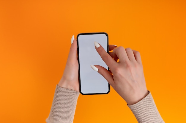 Female hand holding and touching on mobile smartphone with white screen Isolated on Orange Photo template for any images on mobile phone display Layout with easily removable phone monitor background