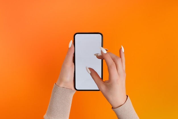 Female hand holding and touching on mobile smartphone with white screen Isolated on Orange Photo template for any images on mobile phone display Layout with easily removable phone monitor background