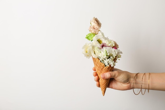 Female hand holding waffle cone with composition of beautiful flowers on white background