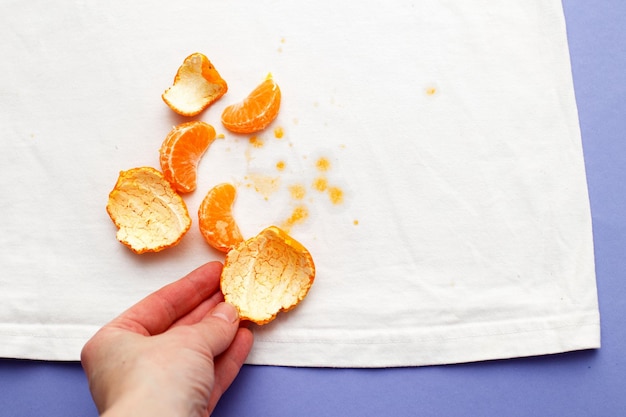 Female hand holding white clothes with ditry stains from fruits mandarin