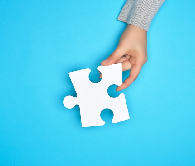 Female hand holding white empty paper puzzle, blue background