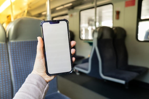 Female hand holding white screen phone in the train Social Network Work and Travel phone with blank copy space screen for your text message New Apps Smartphone with white Screen Mock Up Display