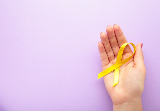 Female hand holding yellow awareness ribbon