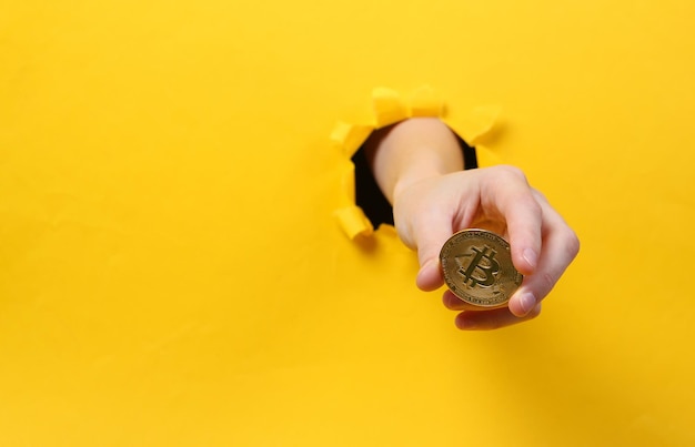 Female hand holds bitcoin through torn hole yellow paper Concept art