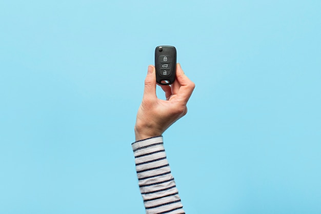 Photo female hand holds car keys on a blue background. concept car, car rental, gift, driving lessons, driving license.