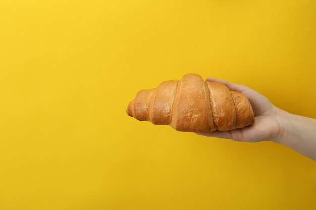 Female hand holds croissant on yellow