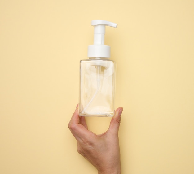 Female hand holds empty plastic container with dispenser for liquid products, soap or shampoo on beige background