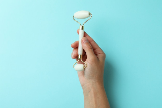 Female hand holds face roller on blue background