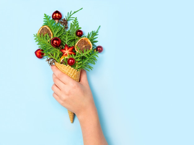 A female hand holds a favela horn with thuja sprigs and Christmas toys on a blue.